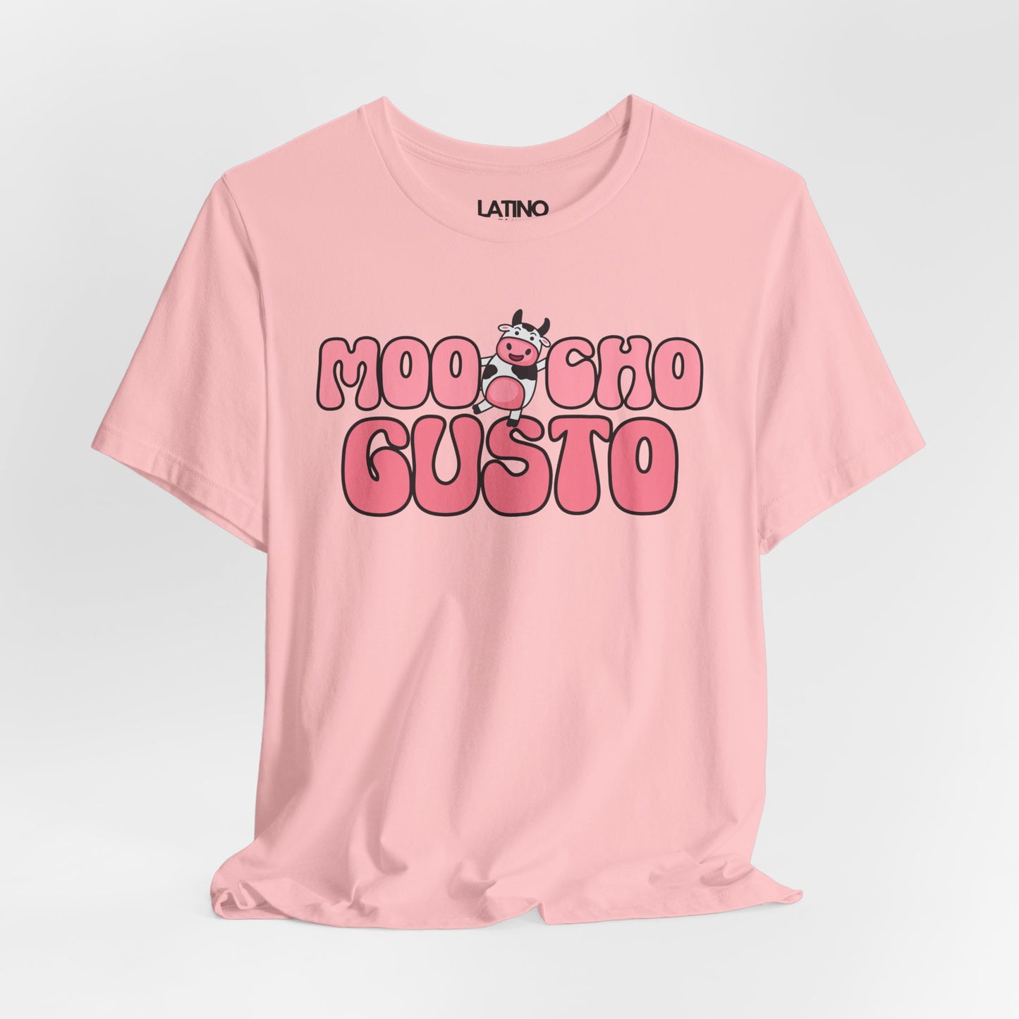 Pink T-shirt with the phrase “Moocho Gusto” in bold bubble letters and a cute cartoon cow between the words