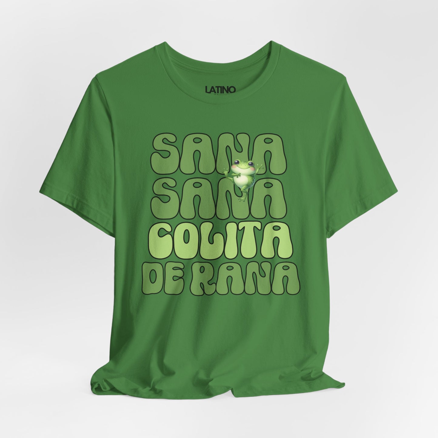 Green T-shirt with the phrase “Sana Sana Colita de Rana” in bold retro letters and a cute smiling frog illustration