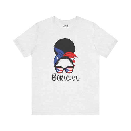A white crew neck t-shirt with a graphic print of a woman's afro hairstyle, sunglasses, and a bandana with the colors of the Puerto Rican flag. The word 'Boricua' is written in elegant script beneath the graphic.