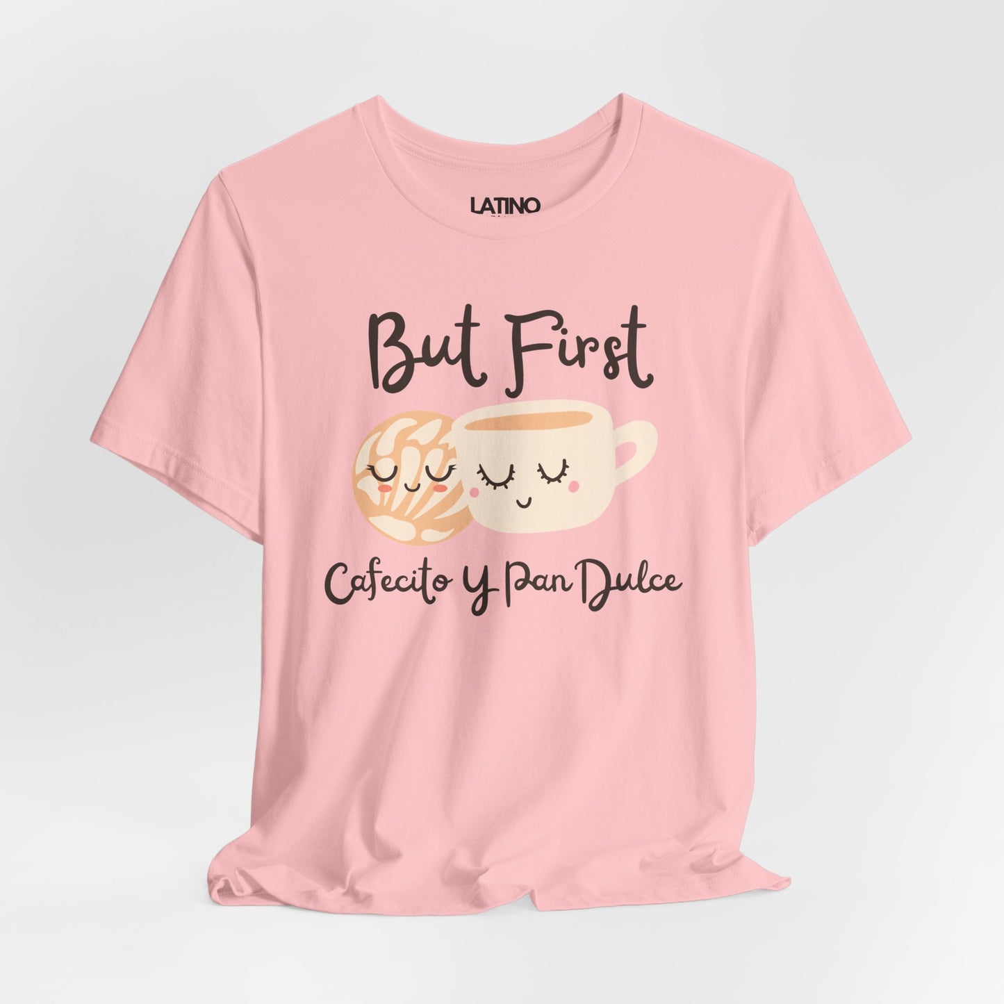 Pink T-shirt with the phrase ‘But First Cafecito y Pan Dulce’ featuring a cute smiling concha pastry and coffee cup illustration
