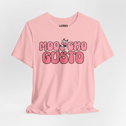Pink T-shirt with the phrase “Moocho Gusto” in bold bubble letters and a cute cartoon cow between the words
