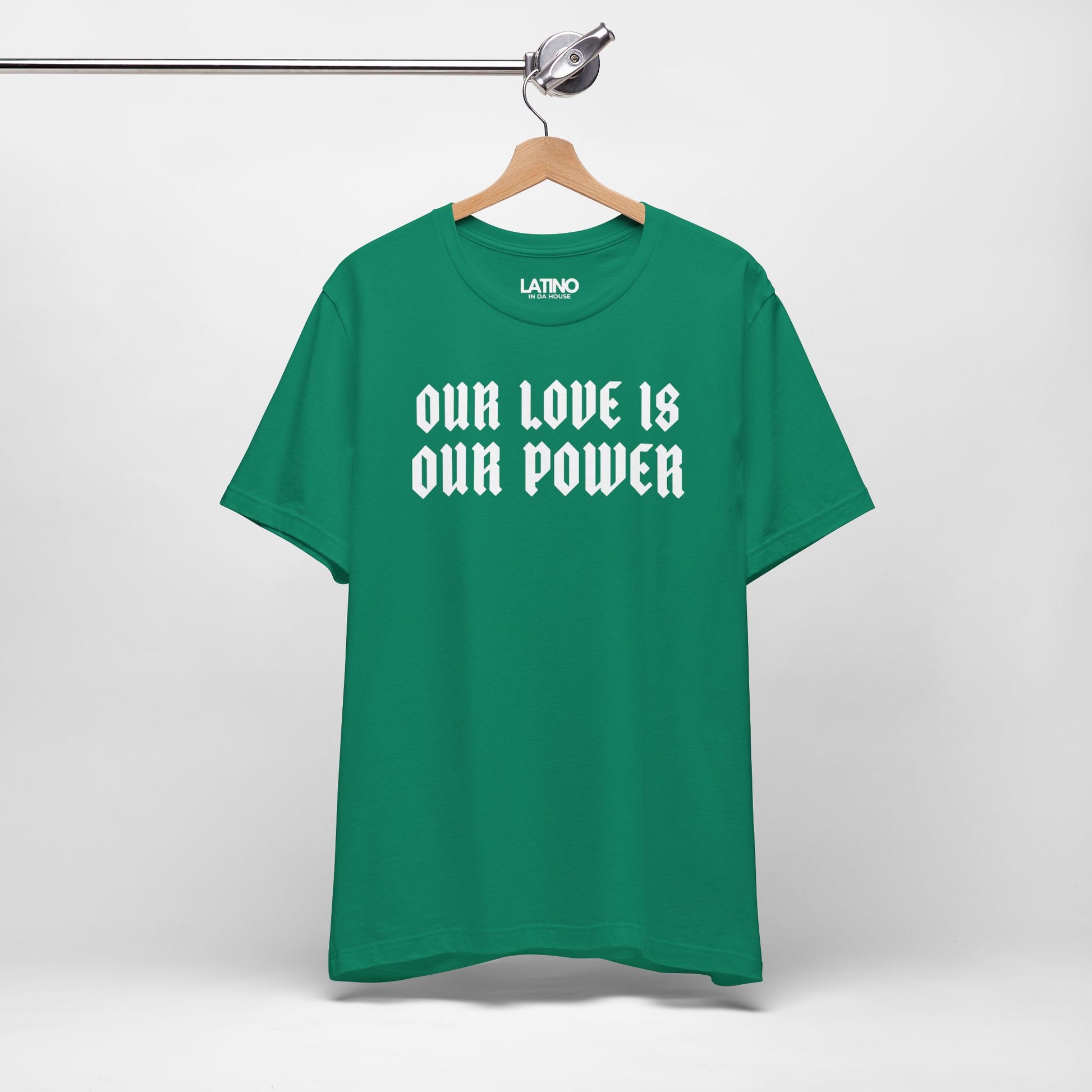 Green t-shirt with 'OUR LOVE IS OUR POWER' text on a hanger against a white background