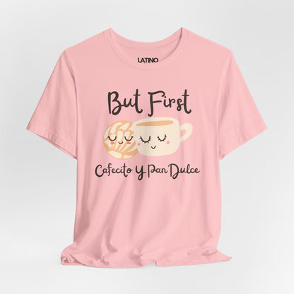 Pink T-shirt with the phrase ‘But First Cafecito y Pan Dulce’ featuring a cute smiling concha pastry and coffee cup illustration